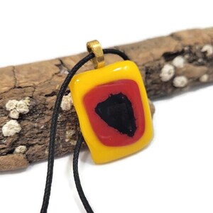 May include: A yellow glass pendant with a red and black geometric design. The pendant is on a black cord.