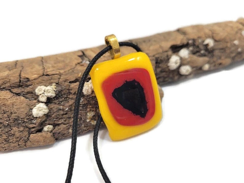 May include: A yellow glass pendant with a red and black geometric design. The pendant is on a black cord.
