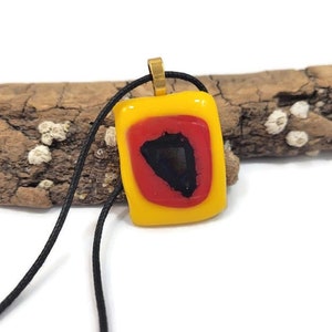 May include: A yellow glass pendant with a red and black geometric design hangs from a black cord.