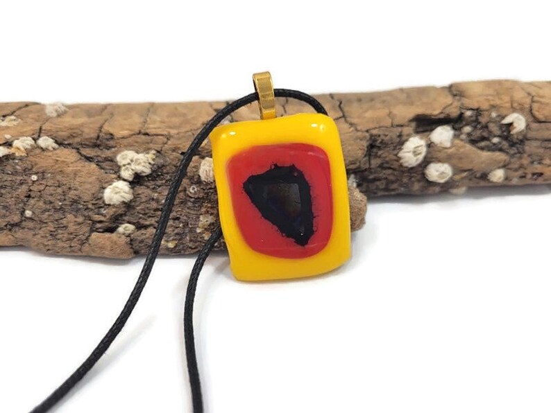 May include: A yellow glass pendant with a red and black geometric design hangs from a black cord.