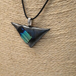May include: A triangular pendant necklace with a black cord. The pendant is a dark gray color with a section of blue and green iridescent material. The pendant is suspended from a silver-colored bail.