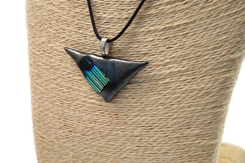 May include: A triangular pendant necklace with a black cord. The pendant is a dark gray color with a section of blue and green iridescent material. The pendant is suspended from a silver-colored bail.