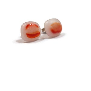May include: A pair of square-shaped earrings with a white background and red and orange swirls.