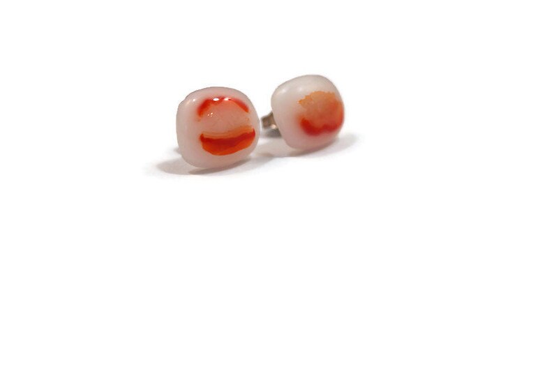 May include: A pair of square-shaped earrings with a white background and red and orange swirls.