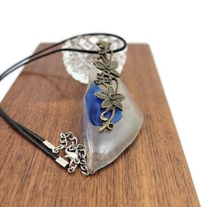 May include: A clear resin pendant necklace with a blue resin swirl and a bronze floral design. The necklace has a black cord and a silver chain.