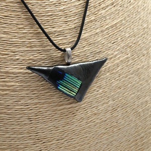 May include: A black triangular pendant necklace with a silver-tone bail and a black cord. The pendant has a section of iridescent green and blue glass. The necklace is displayed on a tan mannequin.