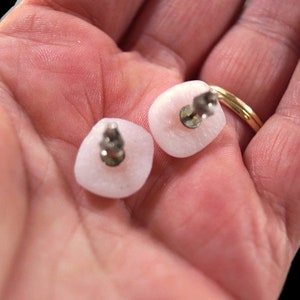 May include: A pair of pink square-shaped earrings with silver posts. The earrings are made of a smooth, opaque material.