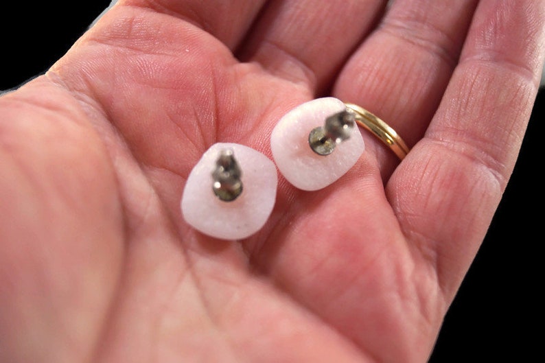 May include: A pair of pink square-shaped earrings with silver posts. The earrings are made of a smooth, opaque material.