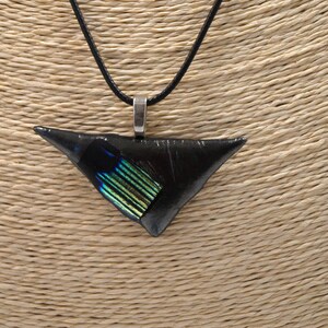 May include: A black triangular pendant necklace with a silver-colored bail and a black cord. The pendant has a section of iridescent green and blue glass. The necklace is displayed on a beige mannequin.