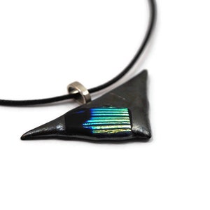 May include: A triangular pendant necklace with a black cord. The pendant is dark gray with a rectangular section of iridescent blue and green glass. The necklace has a silver-colored clasp.
