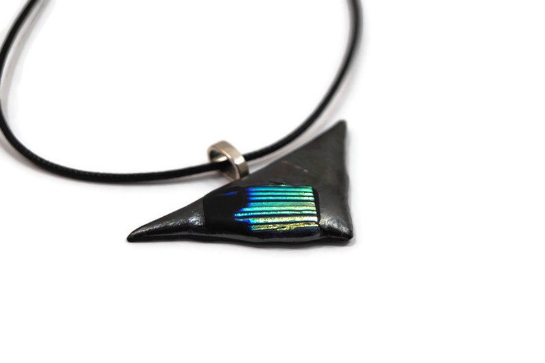 May include: A triangular pendant necklace with a black cord. The pendant is dark gray with a rectangular section of iridescent blue and green glass. The necklace has a silver-colored clasp.