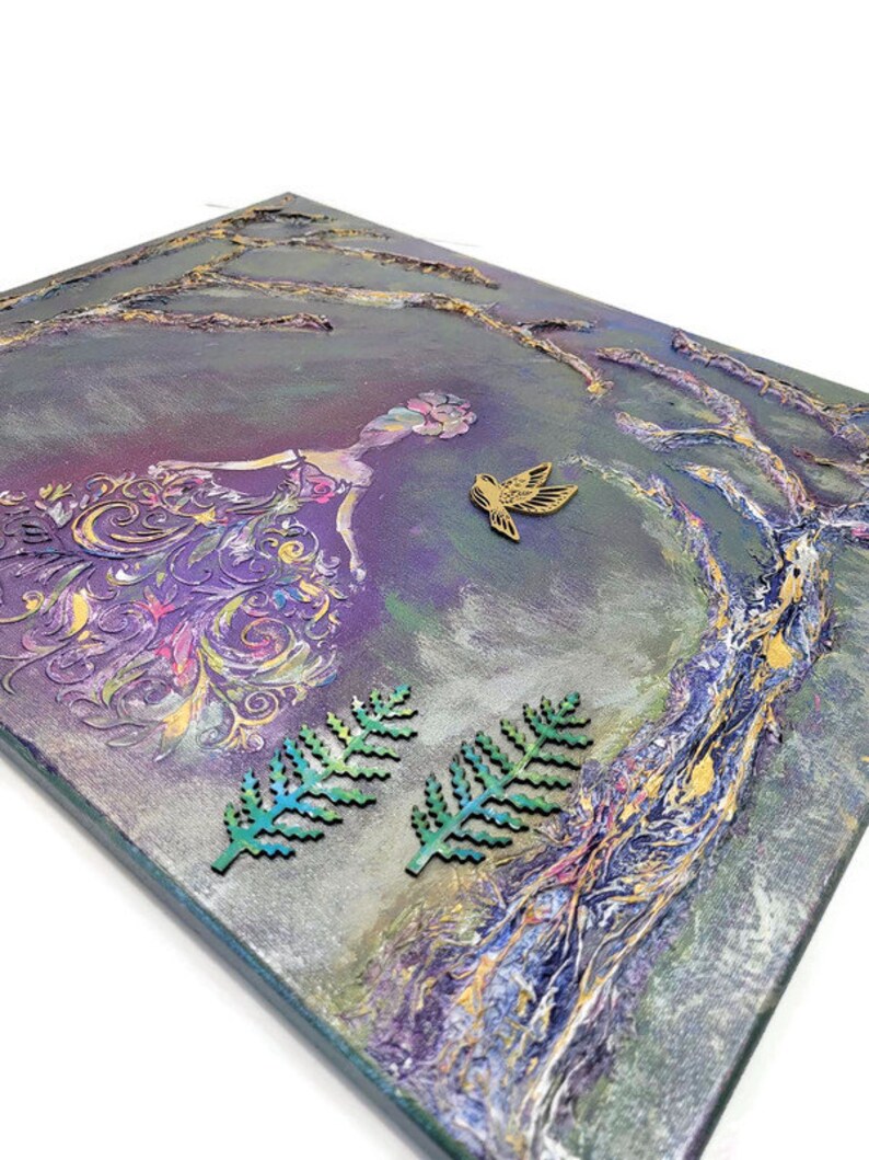May include: Purple and gold abstract painting with a woman in a flowing dress and a bird in flight. The painting has a textured surface and is framed with a wooden frame.