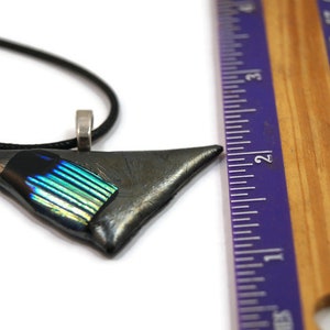 May include: A triangular pendant necklace with a black cord. The pendant is a dark gray color with a section of iridescent blue and green glass. The pendant is approximately 2 inches long.