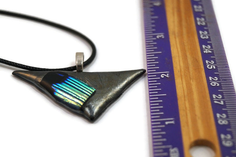 May include: A triangular pendant necklace with a black cord. The pendant is a dark gray color with a section of iridescent blue and green glass. The pendant is approximately 2 inches long.