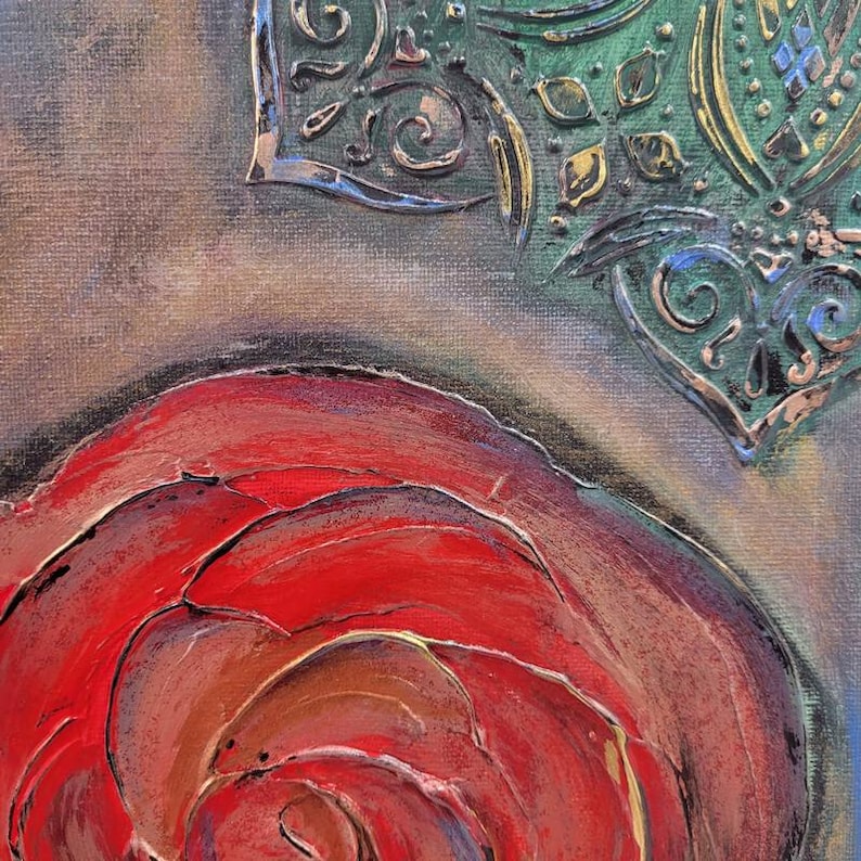 May include: Close-up of an abstract painting featuring a large red rose with textured petals. The artwork includes ornate, metallic-looking embellishments in silver and gold against a green and gray background, creating a layered effect.