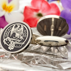 May include: A pair of silver cufflinks with a black and white enamel design. The design features a heraldic eagle with the words "Dread God" around it.