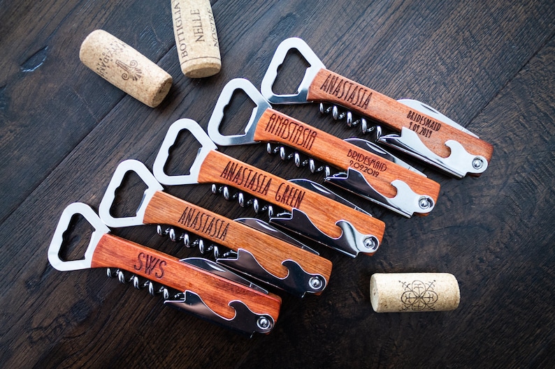 May include: A collection of personalized wooden bottle openers with corkscrews and bottle cap openers. Each opener is engraved with a name or initials. Two corks are also visible.