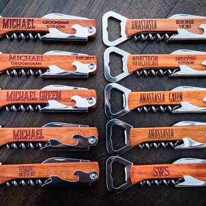 May include: A collection of personalized wooden bottle openers and corkscrews. Each tool features a stainless steel opener, corkscrew, and knife, with custom engraved names and dates. The wooden handles have a wave design.