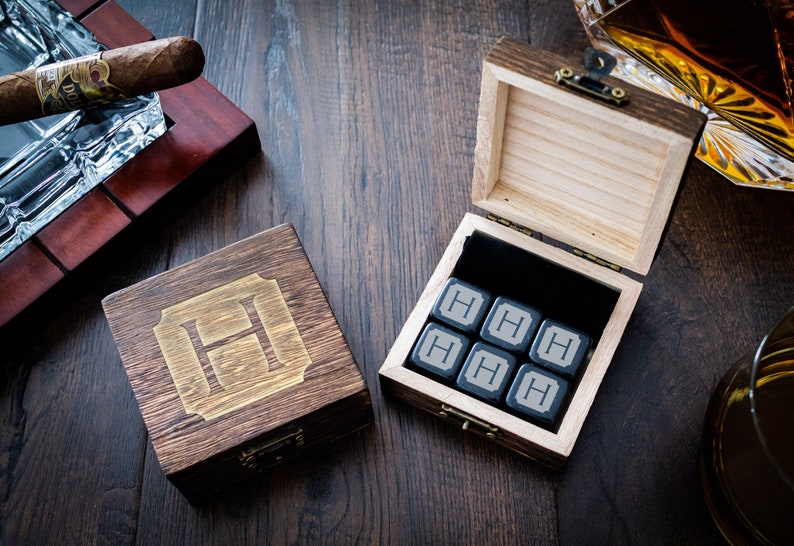 Pu&ograve; includere: Una scatola di legno con un coperchio incernierato, contenente sei pietre per whisky quadrate nere con una lettera H incisa su ciascuna. La scatola &egrave; in legno scuro con una lettera H dorata incisa sulla parte superiore.