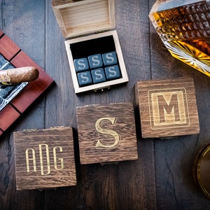 Pu&ograve; includere: Tre scatole di legno con iniziali incise, "ADG", "S" e "M". &Egrave; anche mostrata una scatola con sei cubetti di pietra nera incisi con la lettera "S". Sono anche mostrati una decanter di vetro con liquido ambrato e un bicchiere con liquido ambrato.