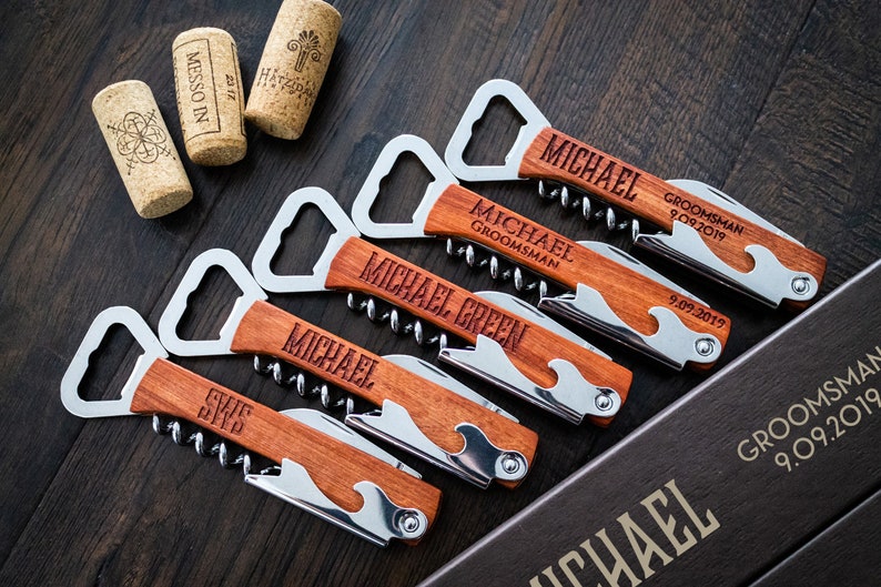 May include: Wooden corkscrews with stainless steel accents, personalized with names and dates. The corkscrews have a bottle opener, knife, and corkscrew. The image also shows wine corks and a box with text.