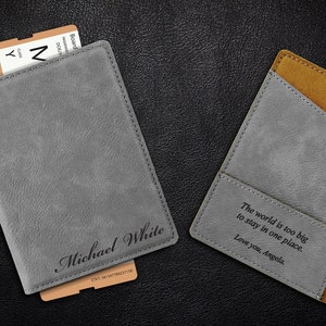 Puede incluir: Dos porta pasaportes grises con detalles marrones. Uno tiene el nombre "Michael White" grabado. El otro tiene el texto "El mundo es demasiado grande para quedarse en un solo lugar. Te quiero, Angela." grabado.