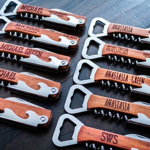 May include: A collection of personalized wooden bottle openers with corkscrews and bottle openers. Each opener has a stainless steel blade and is engraved with names and titles like "Groomsman" and "Bridesmaid".
