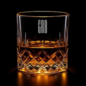 May include: A crystal whiskey glass with a diamond-cut pattern on the lower half, filled with amber liquid. The initials "GRB" are etched in a vertical font on the glass. The glass sits on a reflective surface against a black background.
