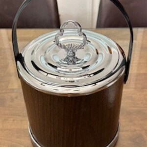 May include: A brown and silver ice bucket with a black handle and a decorative lid. The bucket has a wood-grain pattern.