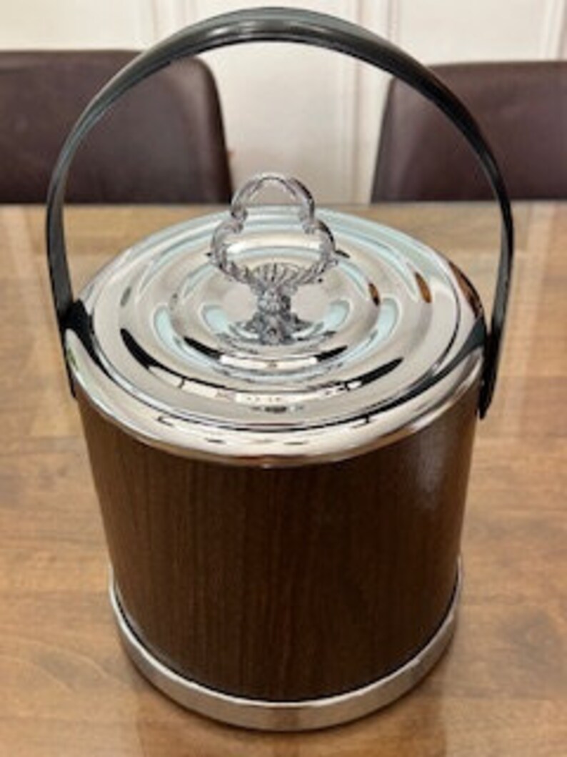 May include: A brown and silver ice bucket with a black handle and a decorative lid. The bucket has a wood-grain pattern.