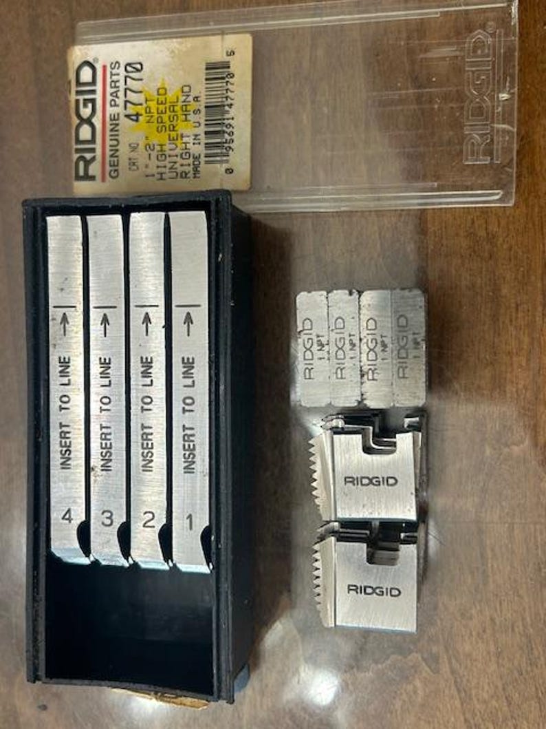 May include: A collection of RIDGID brand plumbing tools. The image shows a black case containing four metal inserts labeled 1-4, and several other metal pieces. A clear plastic case with a label that reads "RIDGID GENUINE PARTS" is also visible.