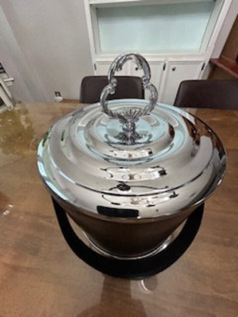 May include: A silver ice bucket with a decorative handle and a black velvet lining. The bucket has a polished finish and a round shape.