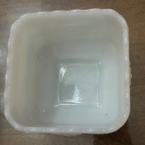 May include: A square white milk glass bowl featuring a scalloped rim with a beaded texture along the top edge. The interior is smooth and glossy, while the exterior walls display a repeating embossed pattern of small raised dots.