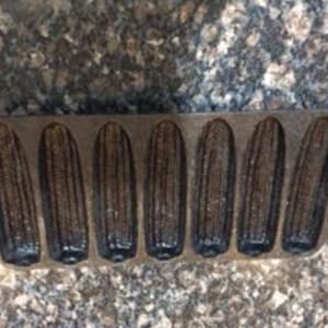 May include: Cast iron cornbread pan with eight individual molds shaped like corn cobs. The pan is dark gray and has a rustic look.