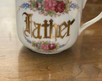 Peut inclure: Une tasse en porcelaine blanche avec un motif floral doré et le mot "Father" en lettres dorées.