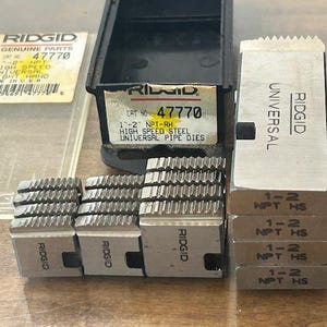 May include: A collection of RIDGID brand pipe dies, including a black storage case and several metal dies. The dies are labeled with sizes and specifications, and the case has a product label with the number 47770.