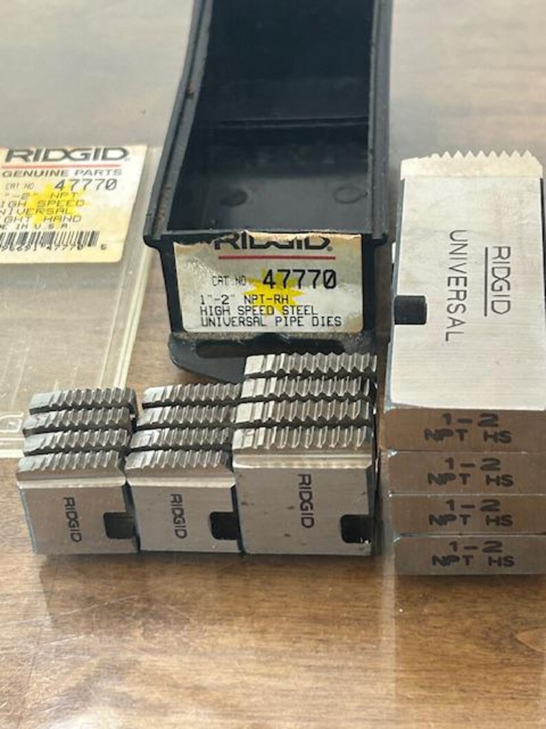 May include: A collection of RIDGID brand pipe dies, including a black storage case and several metal dies. The dies are labeled with sizes and specifications, and the case has a product label with the number 47770.