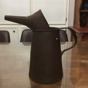 May include: A vintage metal oil can with a spout and a handle. The can is brown and has a worn, rustic look.