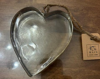 May include: A heart-shaped metal ornament with a reflective silver finish and a jute twine loop for hanging. A rectangular tan paper tag is attached to the twine, featuring the printed text 47 & MAIN HOUSE + HOME in black ink.