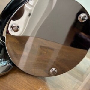 May include: The bottom of a silver round metal bucket with a black leather handle. The bucket has three silver screws on the bottom.
