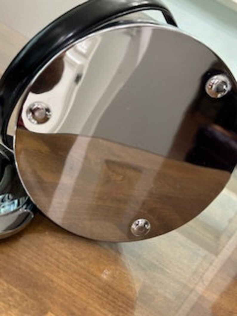 May include: The bottom of a silver round metal bucket with a black leather handle. The bucket has three silver screws on the bottom.