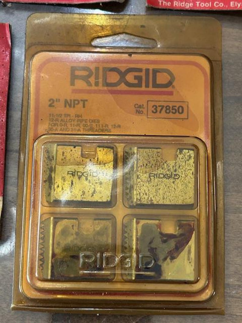 May include: A package of RIDGID 2" NPT pipe dies. The package is a clear plastic with a gold-colored cardboard backing. The dies are gold-colored and are labeled with the RIDGID brand name and the catalog number 37850.