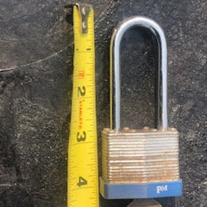 May include: A silver padlock with a blue and silver body and a brass keyhole. The padlock is 2 inches tall and has a PM logo on the bottom.