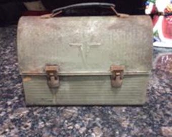 May include: Vintage metal lunchbox with a green paint finish and two latches. The lunchbox has a handle and a slightly curved lid.