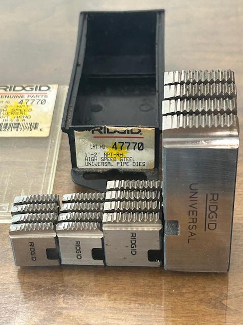 May include: A set of Ridgid universal pipe dies, including a black storage case and several metal dies. The dies are labeled with the Ridgid brand and product information, including "47770" and "High Speed Steel."
