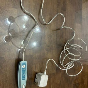 May include: A vintage light blue Sears electric candle lamp timer with a white cord and a white plug-in adapter. The timer has a dial and a switch. The cord is coiled on a brown wooden surface.