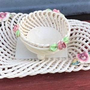 May include: White ceramic basket with a woven design and pink floral accents. The basket is sitting on a matching square plate.