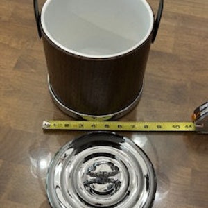 May include: A brown wooden ice bucket with a silver metal base and a silver metal lid. The bucket has a black leather handle.