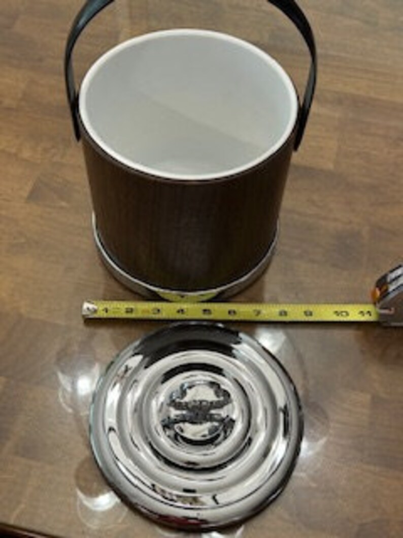 May include: A brown wooden ice bucket with a silver metal base and a silver metal lid. The bucket has a black leather handle.