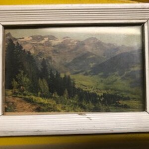 Peut inclure: Une photographie vintage encadr&eacute;e d'une vall&eacute;e de montagne avec des sommets enneig&eacute;s en arri&egrave;re-plan. La photo est dans un cadre en bois blanc au design simple.